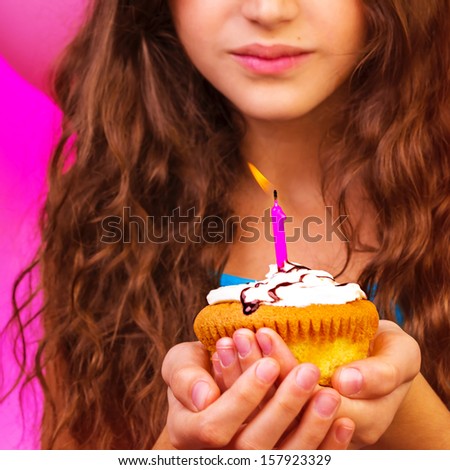 Lovely birthday girl make a wish with sweet festive cupcake in hands, enjoying holiday celebration, having fun indoors, happiness concept