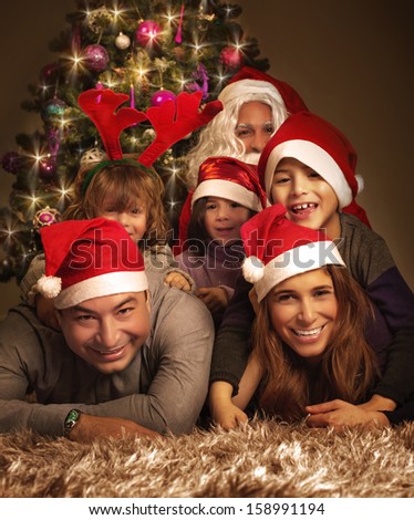Closeup portrait of big happy family with Santa Claus lying down near Christmas tree, holiday celebration, joy and happiness concept