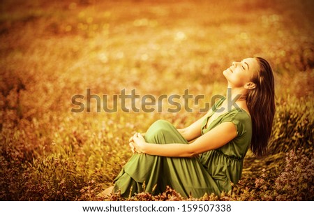 Romantic woman wearing long elegant dress sitting on golden dry field, autumn season, relaxation in countryside, enjoying nature, pleasure concept
