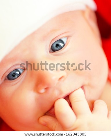 Closeup portrait of cute newborn baby with two fingers in mouth, funny kid face, New Year celebration, happy Christmastime holidays
