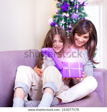 Young brunette mother with teen girl opening Christmas present, excited faces, magical glowing light from gift box, happiness concept