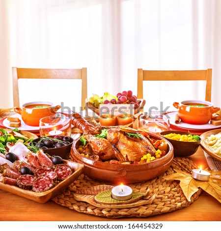 Thanksgiving day dinner, tasty baked chicken on centerpiece of festive table, cold cuts, candle light, greeting card, happy holiday celebration