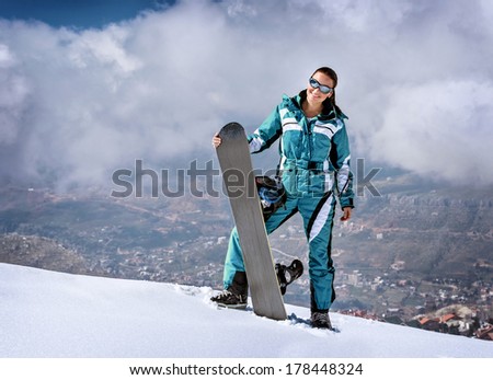 Sportive woman standing on the top of mountain with snowboard in hands, active wintertime holidays, extreme lifestyle concept