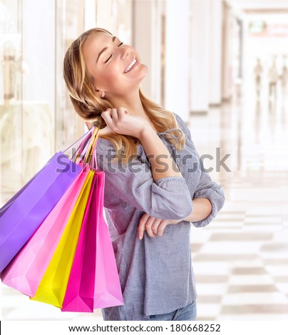 Woman having fun in shopping mall, smiling girl with closed eyes holding in hands colorful paper bags, spending money concept
