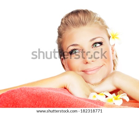 Pretty female lying on massage table at spa salon with fresh frangipani flower in hair, isolated on white background, beauty treatment concept