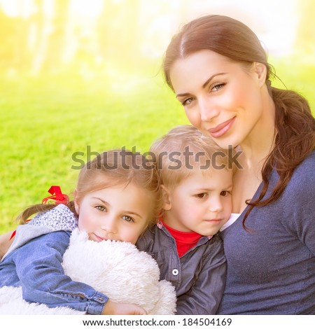 Closeup portrait of beautiful young mother with cute daughter and son sitting on the meadow, bright sun light, summer vacation, love and togetherness concept