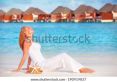 Pretty female on luxury beach resort, sitting on white clean sand and with closed eyes enjoying sunny day, summer vacation concept