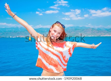 Attractive cheerful woman with raised up hands posing on blue sea background, enjoying summer holidays concept