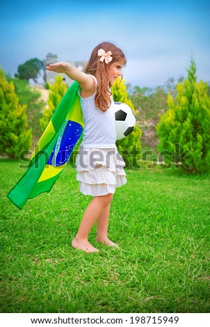 Happy cheerful girl playing with ball on backyard in sunny day, big national Brazil flag, football championship concept