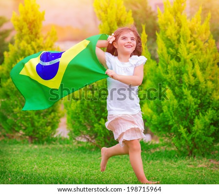 Happy little football fan, cute little girl running on the park with national Brazil flag waving on the wind, sportive childhood, football championship concept