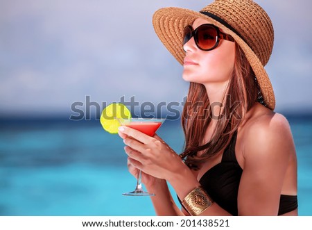 Portrait of stunning woman wearing stylish beach hat and sunglasses drinking cocktail outdoors, summer vacation on Maldives resort