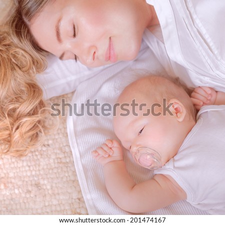 Portrait of sweet newborn child with young mom sleeping on the bed at home, time of day dreaming, healthy lifestyle concept
