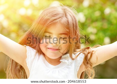 Portrait of attractive little Arabic girl with closed eyes enjoying sunny day, having fun outdoors, pleasure and happiness concept