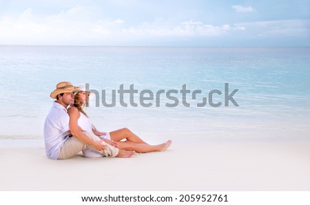 Young family spending summer vacation on romantic beach resort, sitting and hugging on seashore, looking away, affection concept
