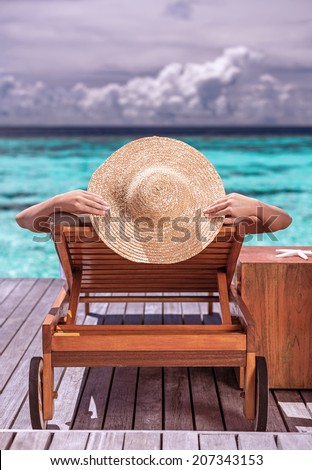 Woman on luxury beach resort, female tanning on sunbed, female wearing a big stylish hat, young girl enjoying beautiful seascape, relaxation on summer travel,  tourism concept