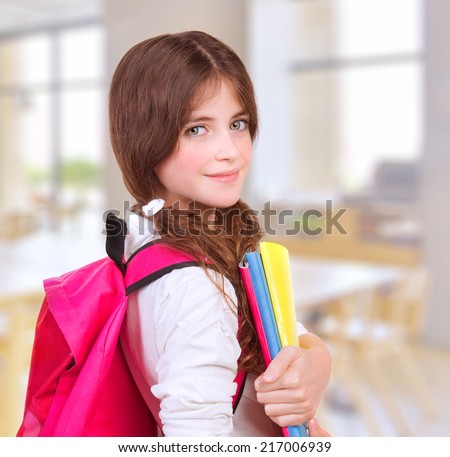 Side view of cute teen girl standing in classroom with colorful books in hands and bright pink backpack on shoulders, preparing to lesson, back to school, knowledge and education concept