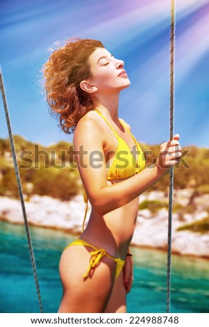 Sexy model enjoying sunny day, woman with perfect body and closed eyes tanning on sailboat, luxury summer cruise concept