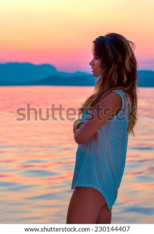 Side view of cute girl enjoying beautiful red and yellow sunset over sea, spending evening on the beach, freedom and enjoyment concept