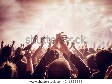 Vintage style photo of a crowd, happy people enjoying rock concert, raised up hands and clapping of pleasure, active night life concept