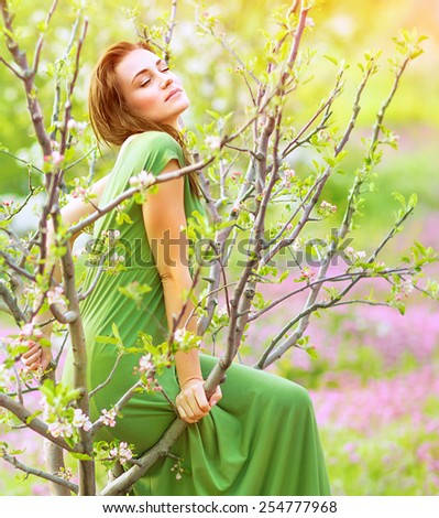 Sensual wood nymph enjoying spring nature, sitting in blooming garden with closed eyes, dreamy girl in long green dress, natural beauty concept