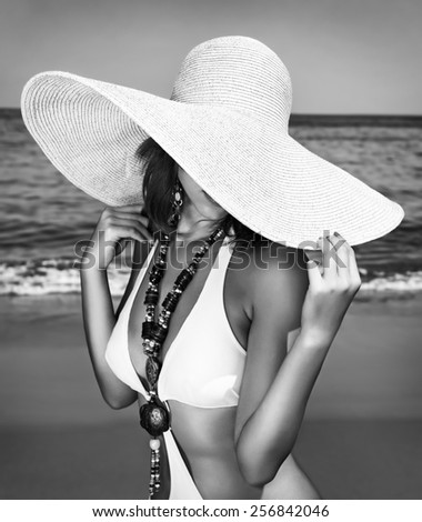 Sexy woman on the beach, black and white photo of fashion model posing on seashore, wearing a big hat, and covers her face, fashionable summer photo shoot