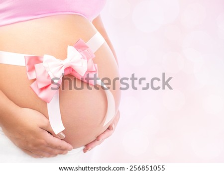Closeup photo of tummy of pregnant woman with pink ribbon bow isolated on blur background, body part, best gift for young family, it\'s a girl concept