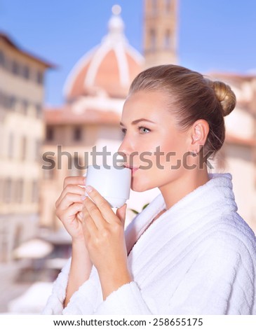Portrait of a beautiful calm woman drinking coffee in hotel room in Florence, standing on the balcony and enjoying wonderful cityscape, tourism and travel to Europe,  Italy