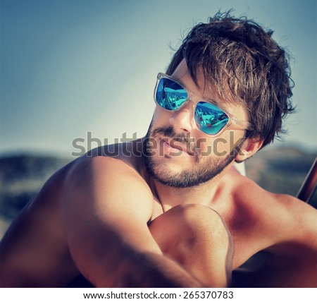 Closeup portrait of handsome man on the beach in mild sunset light, wearing blue stylish sunglasses, summer vacation concept