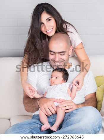 Portrait of happy young family, cheerful parents with cute newborn daughter having fun on the couch at home, love and happiness concept