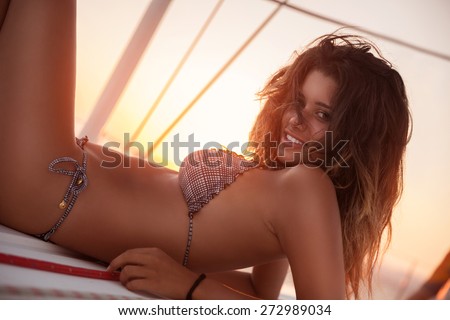 Gorgeous female lying down on sailboat, tanning in mild sunset light, spending leisure time in the sea, luxury summer vacation concept