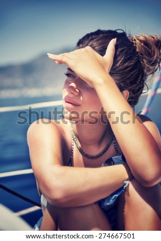 Beautiful woman sitting on the deck of sailboat and cover face from bright sunlight by hand, spending good summer days in the sea
