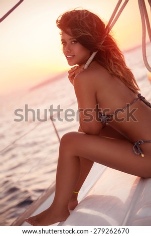 Sexy woman with perfect body tanning on sailboat in mild sunset light, photo shoot in the sea, fashion summer holidays
