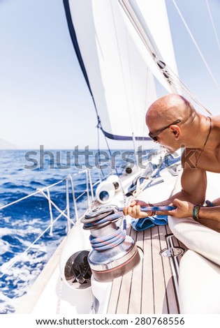 Handsome man working on sailboat, pulling rope, active summer vacation on water transport, having fun in the sea, enjoying water sport
