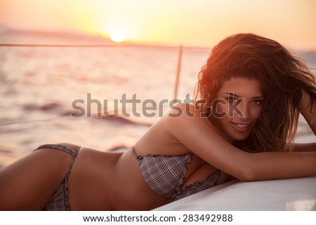 Seductive woman tanning on sailboat in mild sunset light, enjoying traveling along sea, active lifestyle, summer holidays and vacation concept