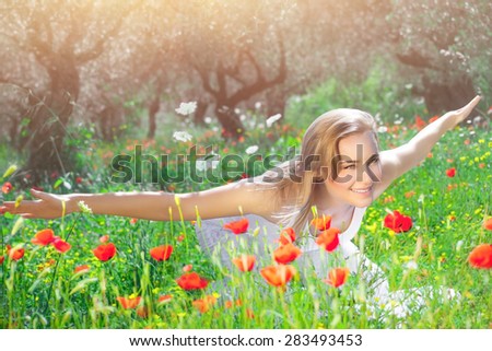 Playful girl having fun on poppy flower field, joyful woman with raised up hands, enjoying wonderful summer nature