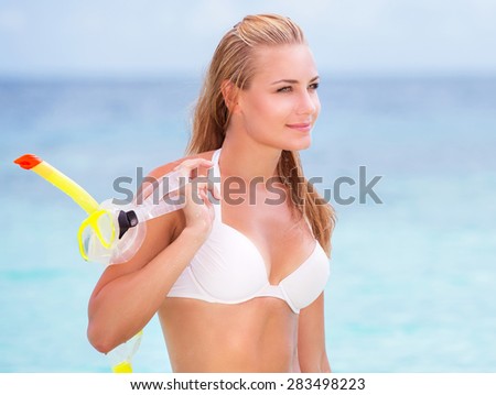 Portrait of happy beautiful girl standing on seashore with a diving mask in hand, having fun on the beach, enjoying summer activities