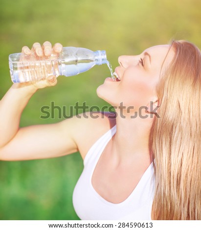 Side view of a beautiful young happy woman drinking water outdoors, refreshment in hot day, fitness activities & healthy eating concept