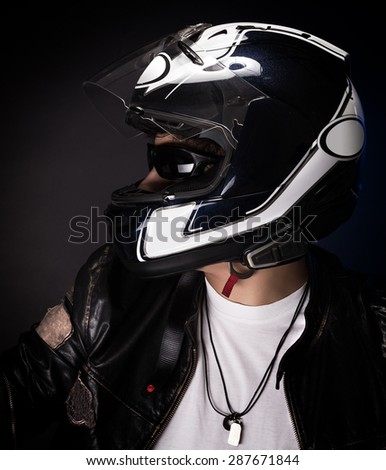 Portrait of stylish biker over dark background, nice teen boy wearing helmet and other bikers outfit, enjoying extreme sport, active lifestyle