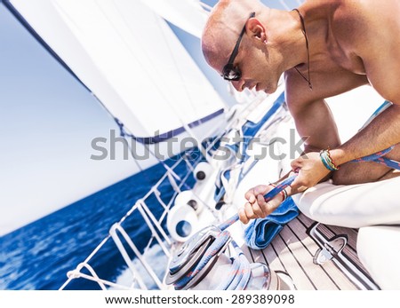 Handsome man working on sailboat, shirtless muscular captain pulling rope on winch, summer time activity, enjoying extreme water sport