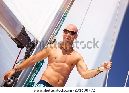 Happy smiling man having fun on sailboat, beautiful shirtless sportive sailor with stylish tattoo enjoying active summer adventure, luxury beach holidays