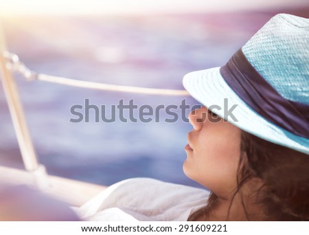 Beautiful woman relaxing on the deck of sailboat in sunny day and tanning, enjoying peaceful luxury summer vacation on a sea cruise