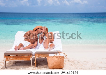 Happy couple kissing on beach resort, tanning on sunbed and eating tasty sweet ice cream, enjoying summer time on beautiful sea coast