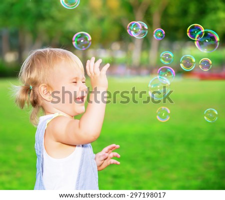 Happy child having fun in the park, cute blond baby girl playing with soap bubbles on the yard, joyful little kid enjoying outdoors game