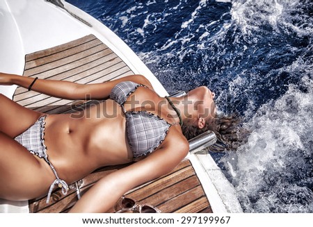 Beautiful woman in summer vacation, gorgeous model with perfect body extremely lying down on the board of sailboat and tanning, having fun in the sea