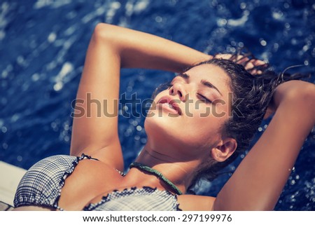 Portrait of woman tanning on the sailboat, lying down with closed eyes and relaxing on the board, enjoying bright sun light, spending summer vacation with pleasure