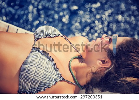 Woman tanning on the sailboat, wearing stylish swimsuit, lying down and relaxing on the board, enjoying bright sun light, spending summer vacation with pleasure