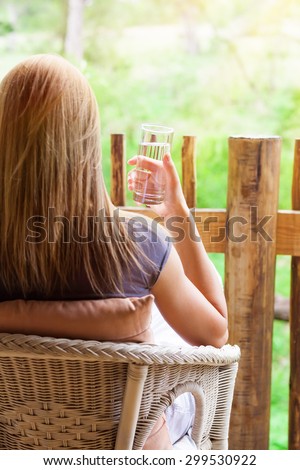 Calm woman relaxing outdoors, back side of female sitting on the chair on terrace, drinking water and enjoying beautiful nature view