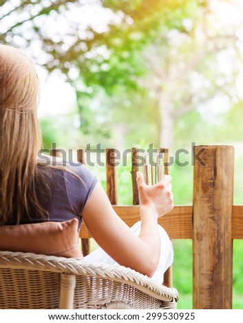 Calm woman relaxing outdoors, back side of female sitting on the chair on terrace, drinking water and enjoying beautiful nature view