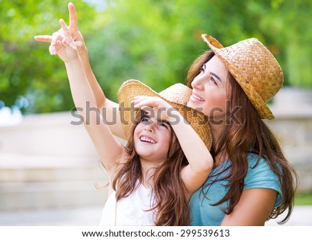Happy mother and daughter spending time together outdoors, pointing fingers and enthusiastically looking up, with pleasure spending time in countryside