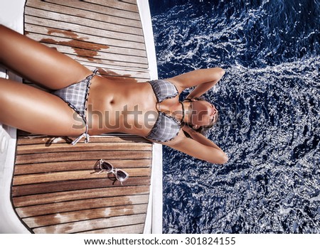 Beautiful woman tanning on sailboat, extremely lying down is on board and enjoying the sea spray, spending luxury summer vacation